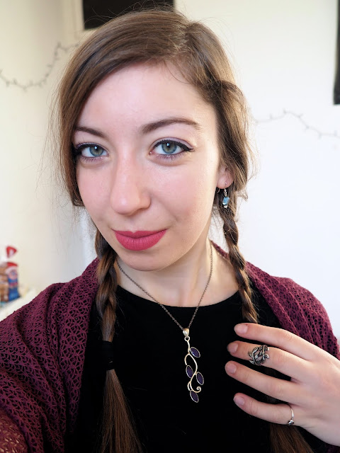 Anna Frozen Disneybound outfit details of small blue stone earrings, purple leaf design pendant necklace, and silver leaf ring, with bright pink lipstick