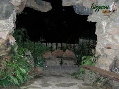 Detalhe da entrada da gruta de pedra, de dentro para fora, com o banco de madeira, o piso de pedra com pedra moledo, o banco de pedra e o piso de pedrisco com execução do paisagismo.