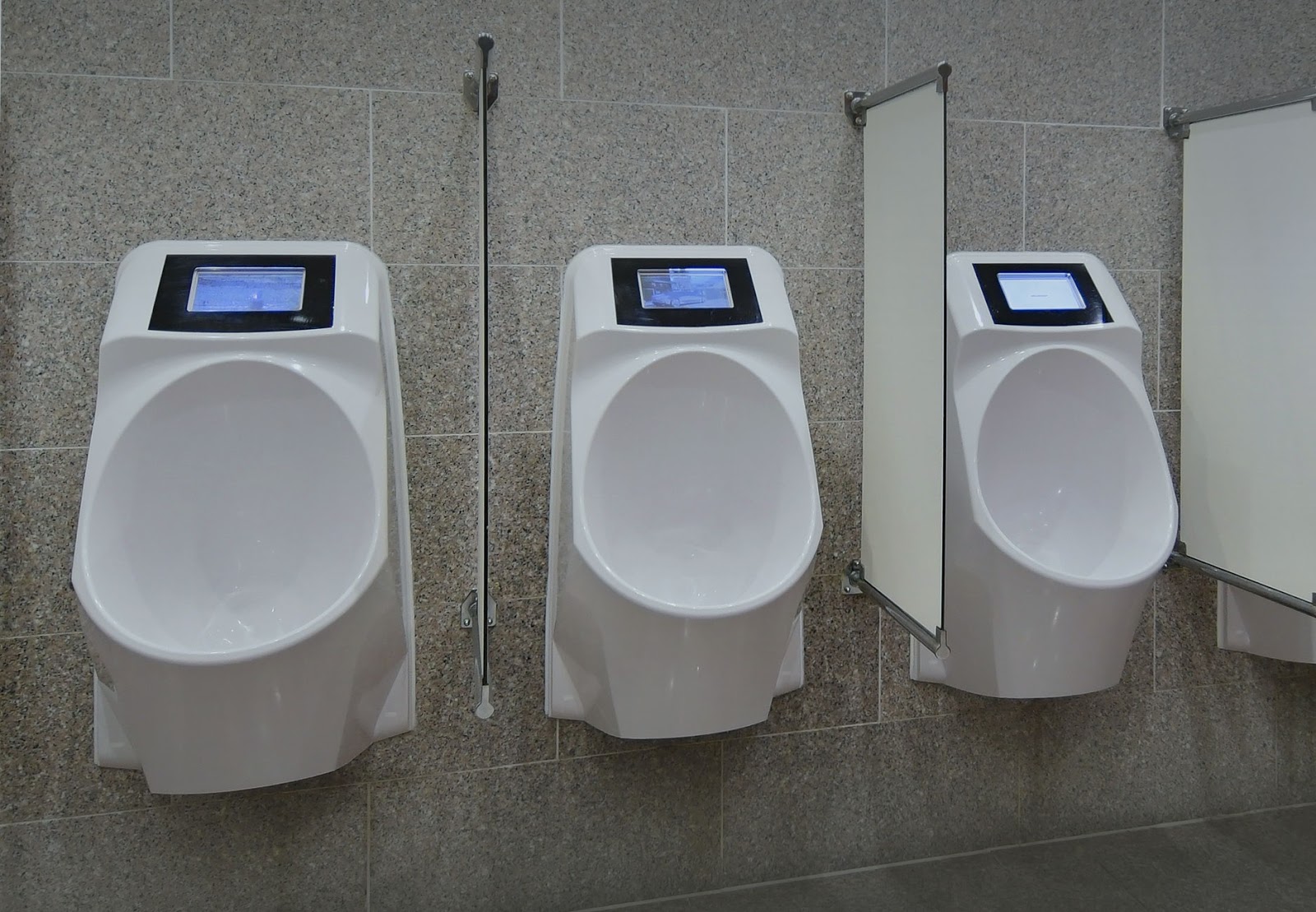 A picture showing three urinals in a bathroom, each with an integrated display above the port hole