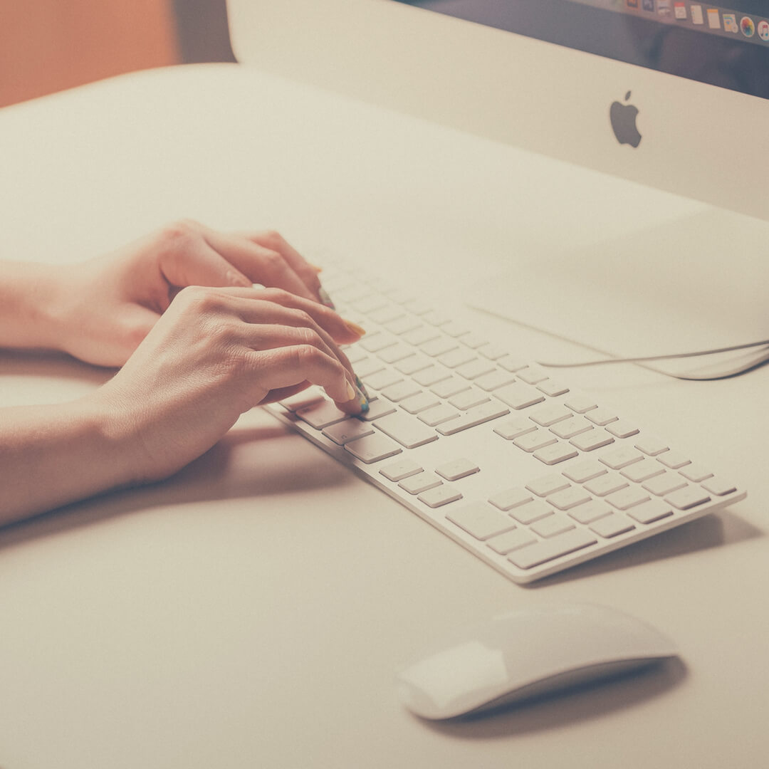 A woman's hands rest on an iMac keyboard. 