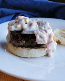 burger patty on top of english muffin bottom with creamy bacon gravy spilling off the side of the burger