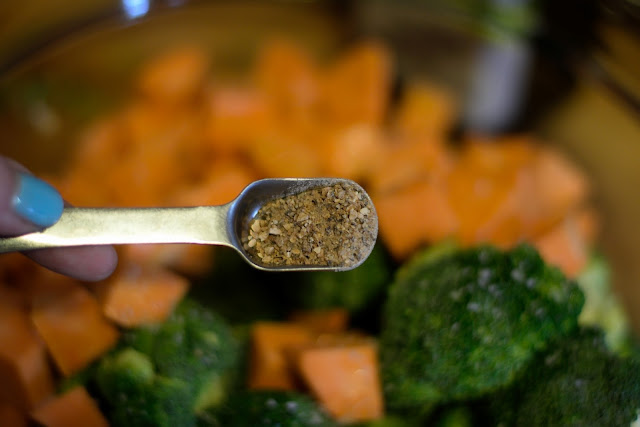 Lemon pepper seasoning being added to the bowl of prepped broccoli and sweet potatoes. 