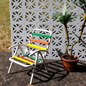 One-tweltfh scale modern miniature garden chair and plant in front of a miniature breeze block wall.