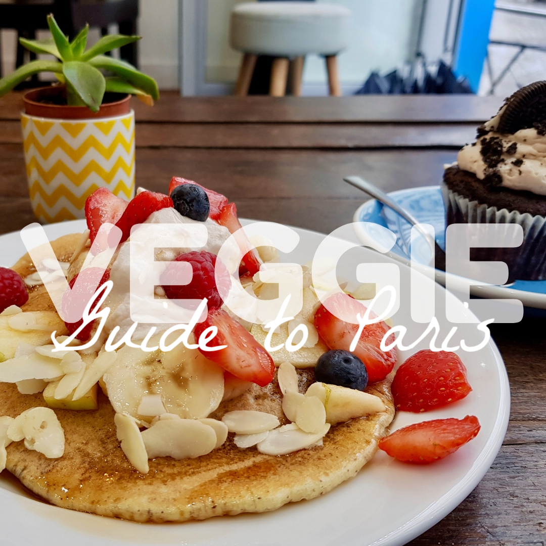 a stack of pancakes, topped with fruit, sit on a wooden table, cupcake with Oreo on top in background