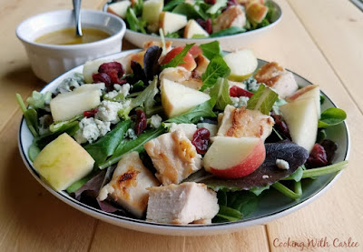 The crunch of fresh apples, the sweetness of dried cranberries, savory chicken and cheese, and fresh greens come together in this great salad that helps bridge the seasons when you still want something light but fall flavors are calling your name! The homemade dressing is perfect for all kinds of salads as well! side view of bowls of fall dinner salad with chunks of apple, chicken, cranberries, cheese and homemade vinagriette