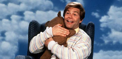 Al Franken, in his role Stuart Smalley, hugging a teddy bear