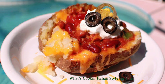 this is a chili topped baked potatoes loaded with shredded cheeses, olives, sour cream and chopped tomatoes