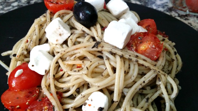unos espaguetis hechos con los ingredientes de la ensalada griega: tomate, queso feta y aceitunas negras