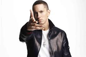 Rapper Eminem pointing toward you with an open right hand, wearing a white tee shirt, black leather jacket, and a cross around his neck
