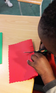 Um aluno a cortar a cartolina vermelha para fazer o seu postal