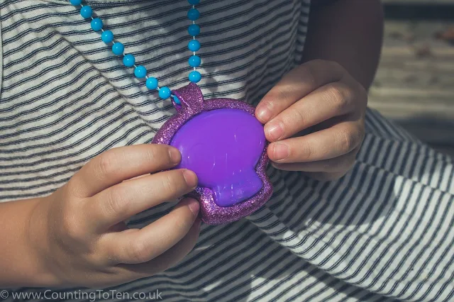 A close up of a child's hands holding a large purple skull pendant on a blue bead necklace