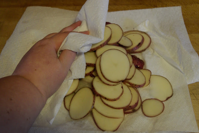 The sliced potatoes being pat dry with paper towels. 