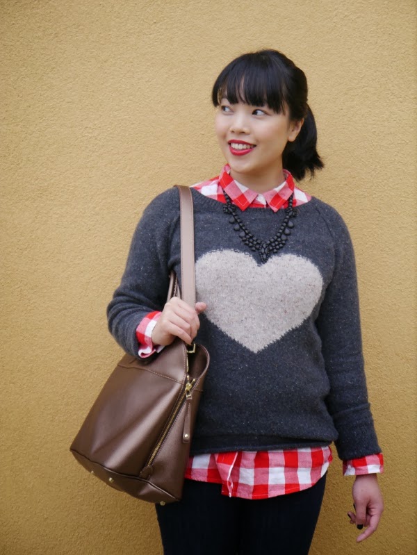 Charcoal grey heart intarsia sweater layered over red check shirt and black matte statement necklace.