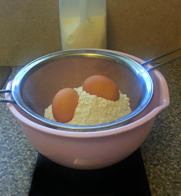 Eggs and flour in seive over mixing bowl