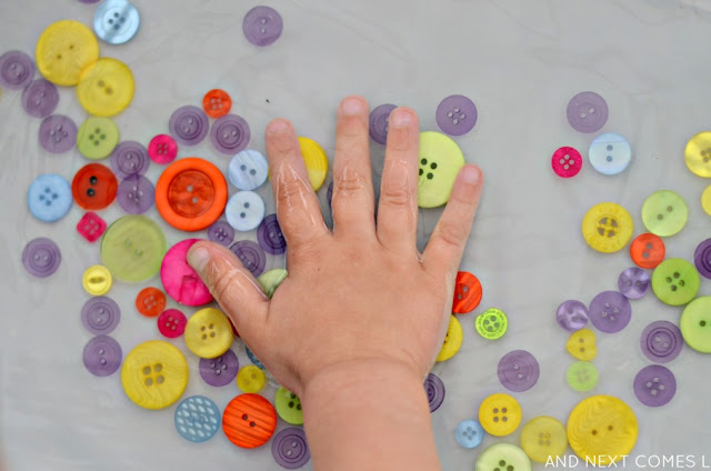 Child's hand in a water & button sensory bin