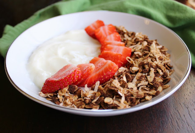 close up of bowl of yogurt with sliced strawberries and chocolate coconut granola