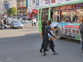 young woman carrying a poodle across a street intersection in Mudanjiang, China