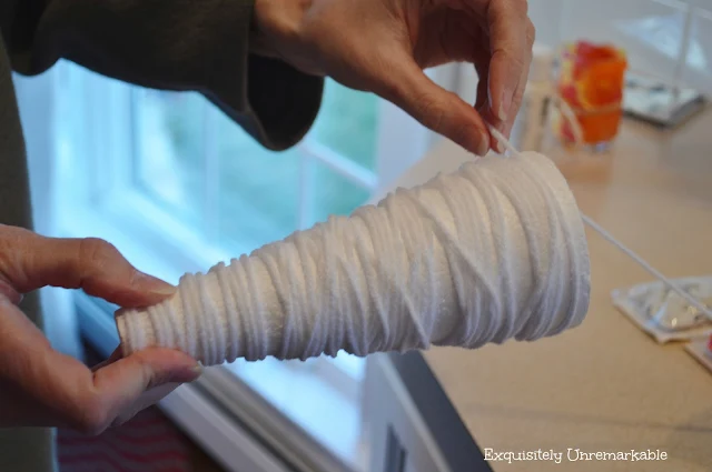 A hand holding a foam cone and wrapping white yarn around it