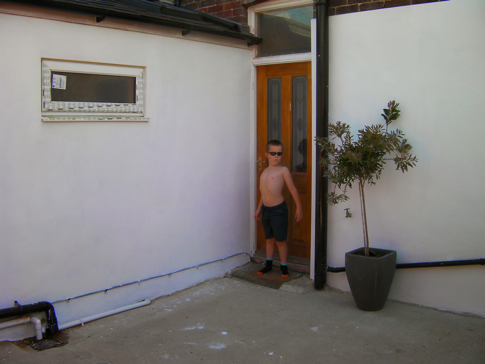 boy in sunglasses by newly painted back yard walls rendered house walls white masonry paint bottlebrushe tree in a pot