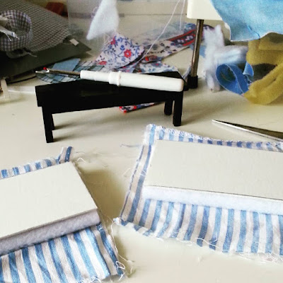 Pieces of fabric, card and padding on a table with a pair of scissors and a seam ripper (which is sitting on a one-twelfth scale black bench seat).