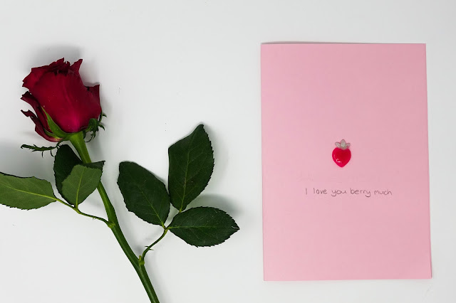 A red rose and a pink card with a small gel a peel strawberry and message
