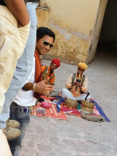 Man giving a thumbs-up with a snake charmer in the background at Amber Fort in Jaipur India