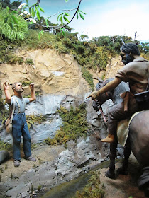 Diorama of a 19th-century man standing in the bush with his hands up,in front of a Maori on a horse.