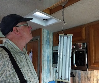 light change in process man looking at old RV light fixture hanging from ceiling