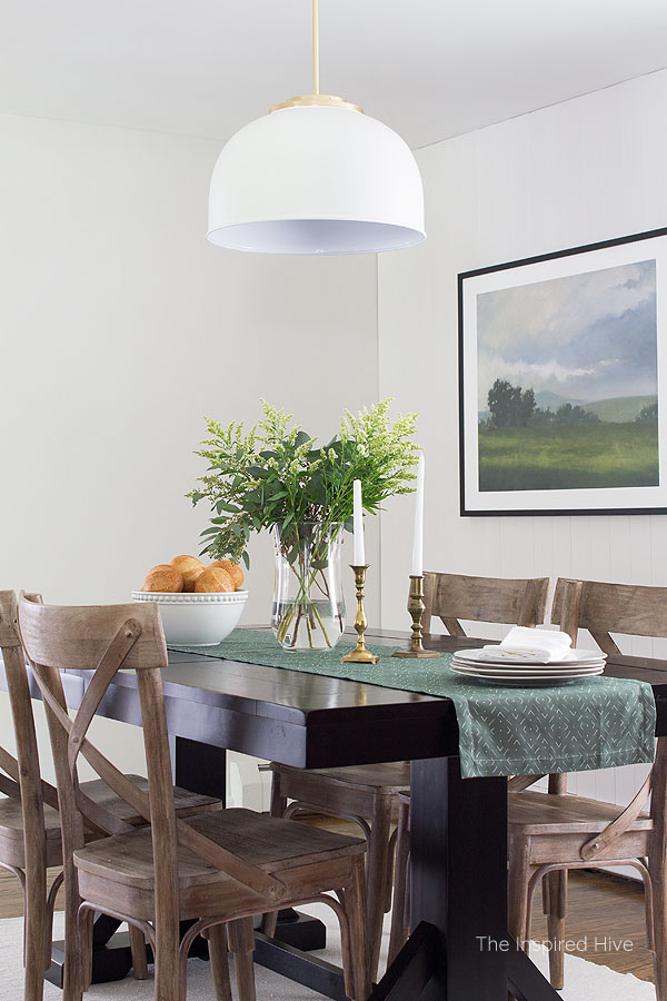 Farmhouse dining room with white vertical tongue and groove, black table, whitewashed wood chairs, large landscape art, and green table runner. Modern traditional style decor.