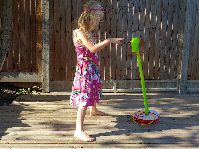 A girl with a pink hoop on her head throwing another hoop over the head of a green plastic worm