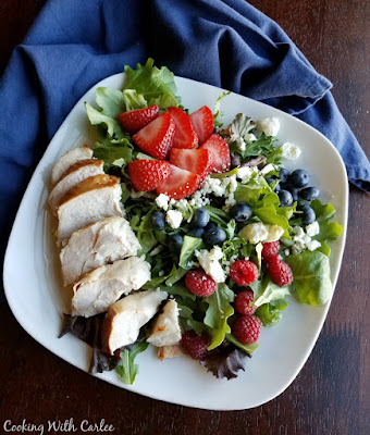 This dinner salad is perfect for Memorial Day, the 4th or July or any day! It is full of berries, cheese, greens, and chicken. There is also a homemade dressing recipe if you'd like! plate of greens with chicken breast, raspberries, strawberries, blueberries and crumbled cheese