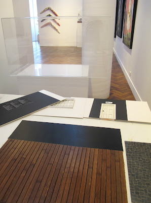 Various walls and floor of a miniature room, laid flat on a table in  a gallery, in front of an empty display cabinet.