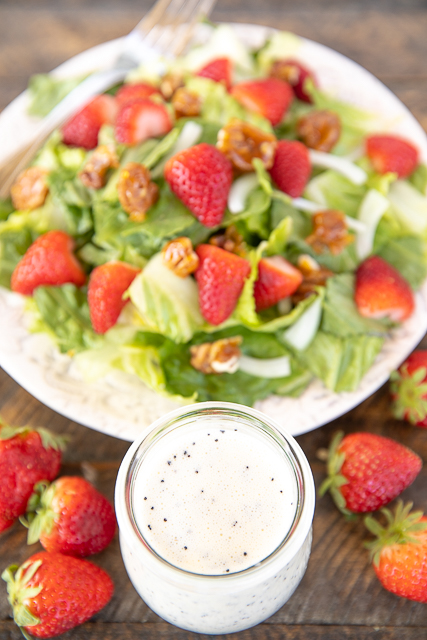 Strawberry Salad with Poppy Seed Dressing and Homemade Candied Pecans Recipe - seriously delicious! We love this for a quick side at lunch or dinner. Romaine, strawberries, Vidalia onions tossed in a quick homemade dressing made from mayonnaise, sugar, sour cream, milk, cider vinegar and poppy seed. Top the salad with some easy candied pecans. We love this with grilled chicken, quiche, and sandwiches. A family favorite! #salad #summer #strawberrysalad poppy seed dressing in a jar with strawberry salad in the background