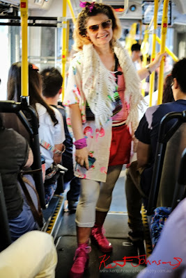 Flora in Pink singlet and Red shorts, white jacket scarf and leggings with pink runners - photographed on the 426 bus on City Road by Kent Johnson.