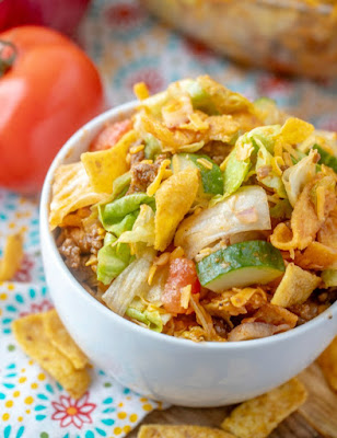 Frito salad is a fun twist on a taco salad. It is loaded with flavor and is perfect for potlucks, but also makes a fun dinner main dish. The homemade catalina salad dressing is easy to make and the salad is packed full of goodies. looking down at a bowl of frito taco salad, served and ready to eat