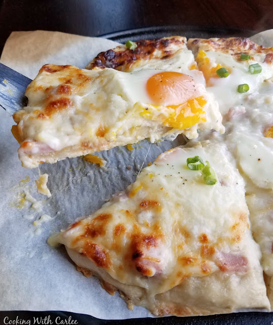 The flavors of the classic French sandwich make an excellent pizza. Croque madame has never been so fun to eat! lifting slice of creamy white pizza with gooey egg on top