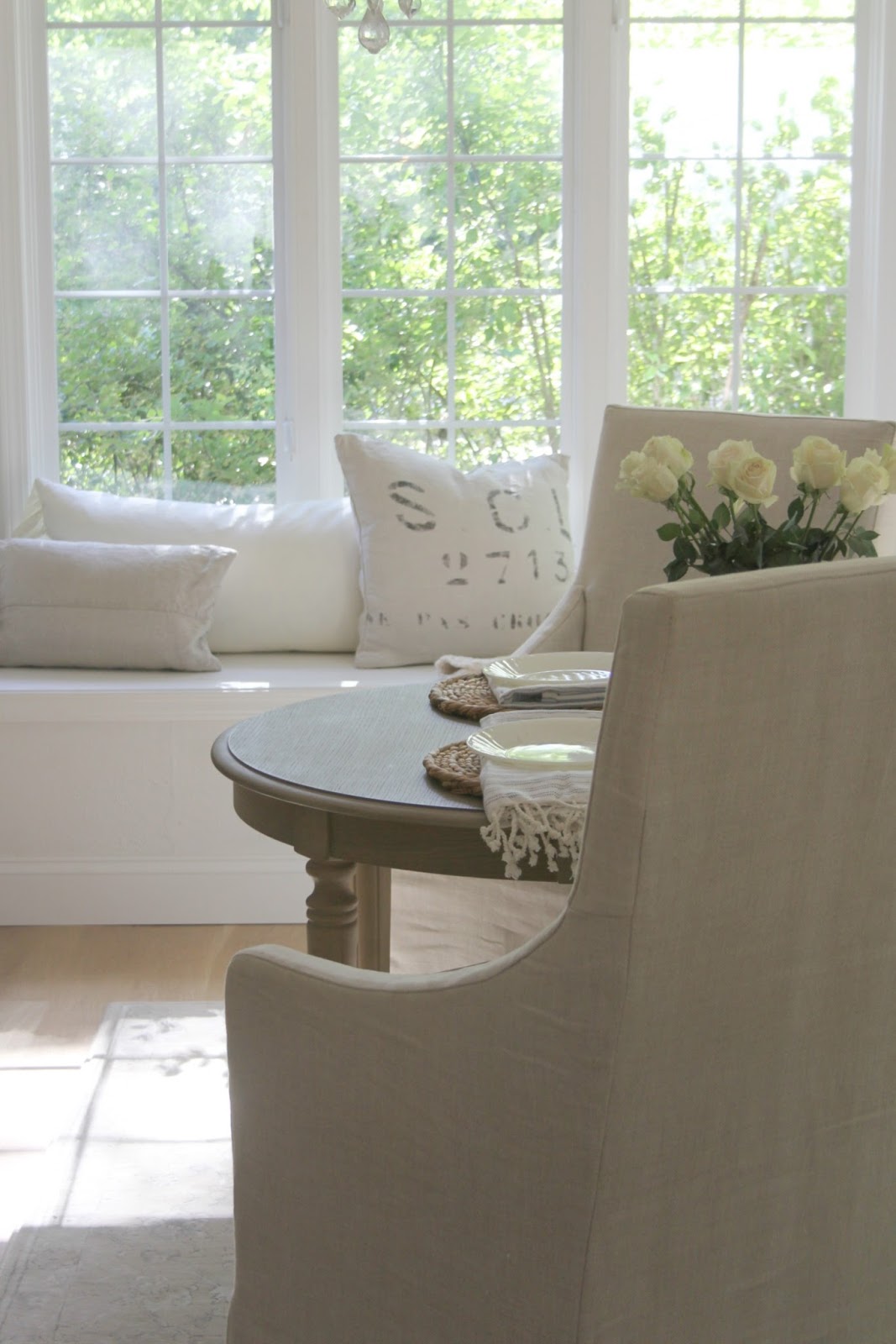 Serene breakfast dining area of kitchen with window seat. Belgian linen pillows and slipcovered arm chairs. Find low cost timeless decorating ideas on Hellolovelystudio!