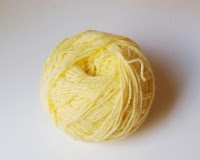 A hand wound ball of lemon yellow 8 ply (DK) acrylic yarn sits upon a white background.
