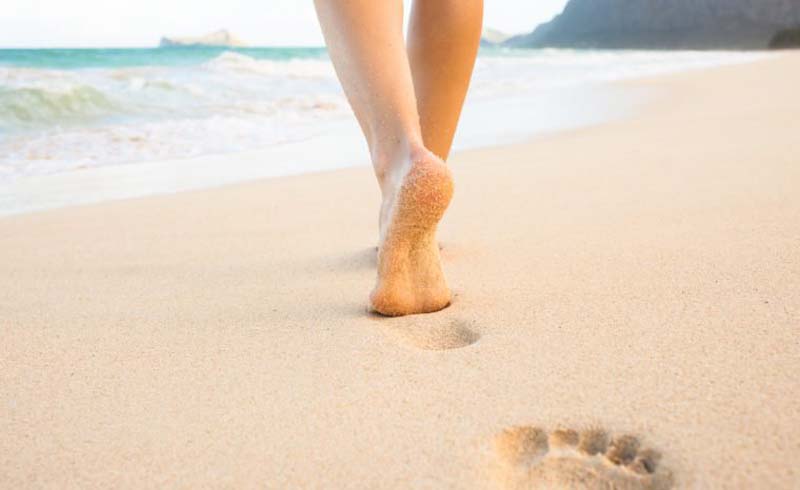 Beach travel - woman walking on sand beach leaving footprints in the sand. Closeup detail of female feet and golden sand on Maui, Hawaii, USA.