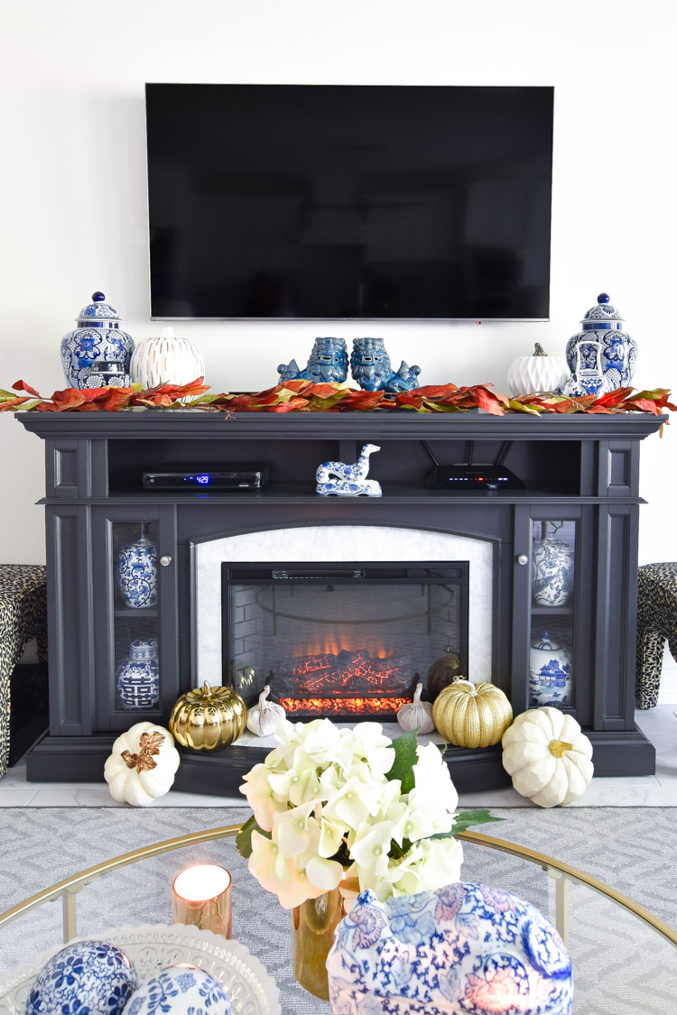 Foo dogs, ginger jars and other blue and white chinoiserie decor paired with white and gold pumpkins on a gray marble fireplace TV stand. Foo dogs, ginger jars and other blue and white chinoiserie decor paired with white and gold pumpkins on a gray marble fireplace TV stand.