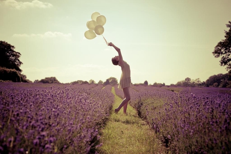 Mujer joven jugando con globos de colores en un camino que divide un campo de lilas.