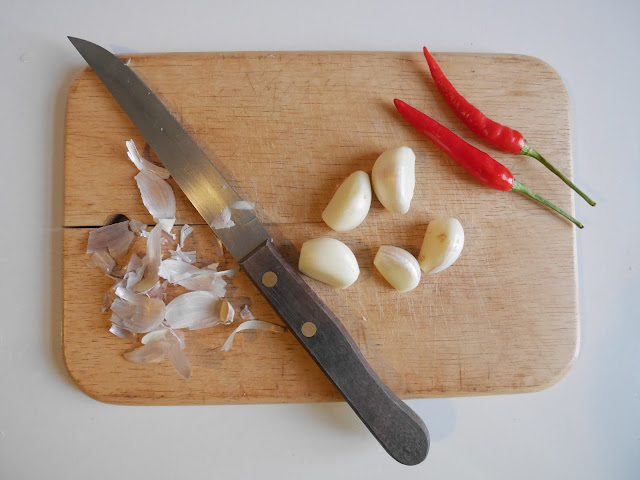 peeled garlic on a cutting board next to Thai chilis