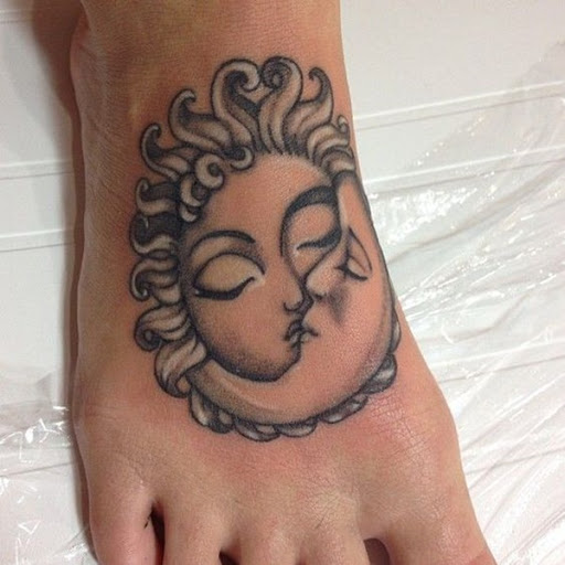 Este preto e cinza tatuagem mostra uma personificação do sol e da lua beijando e é representada na parte superior do utente de pé direito.