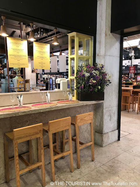 Three wooden bar stools at a kitchen counter decorated with flowers in a market hall.