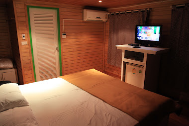 Oak-colored bedroom with a satellite TV and a refrigerator.