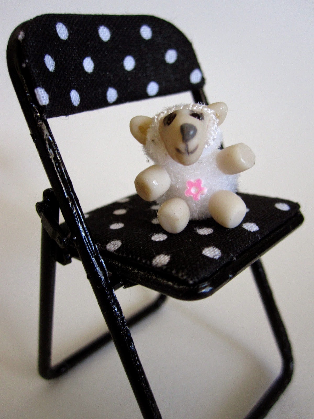 Modern dolls' house miniature stuffed toy sheep sitting on a miniature black and white spotted folding chair.