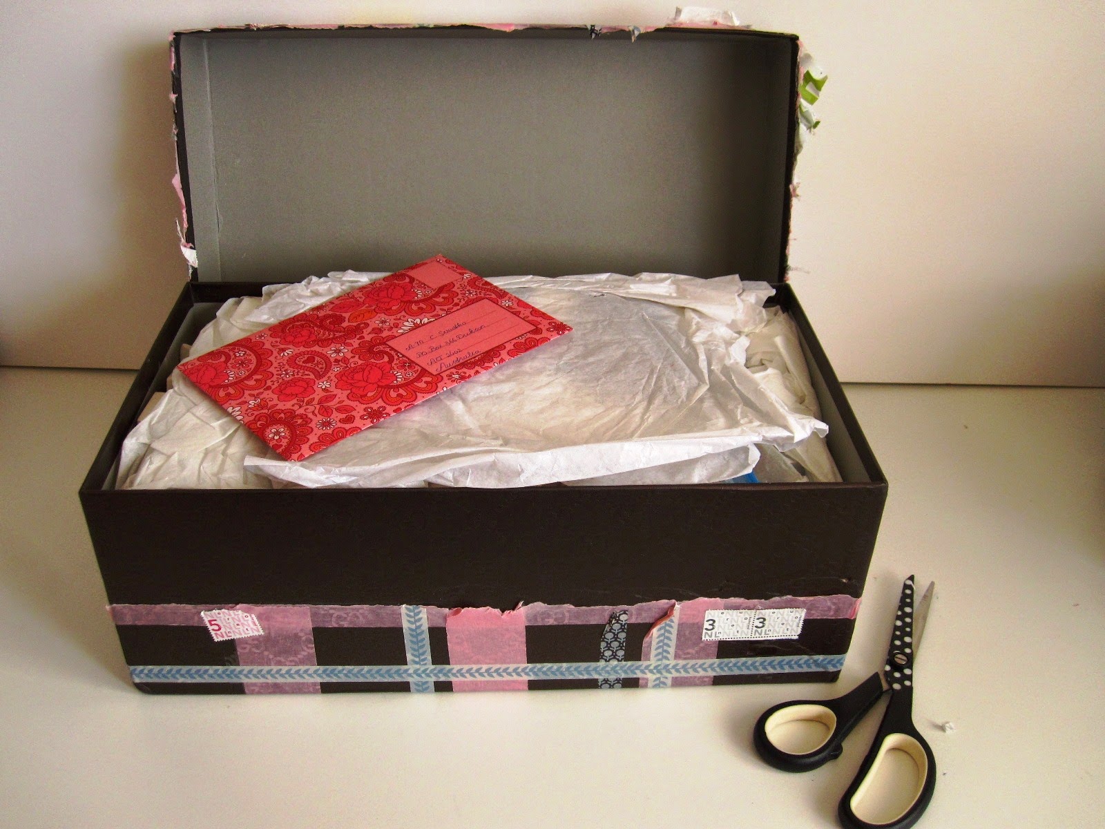 Large washi tape-wrapped shoebox with lid off, showing tissue paper and a colourful envelope on top of it.