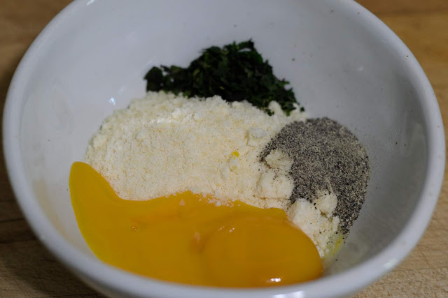 The egg yolks, grated parmesan cheese, pepper, and fresh basil in a mixing bowl.