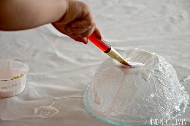 Painting Mod Podge on a plastic wrapped glass bowl as part of a fine motor skills craft
