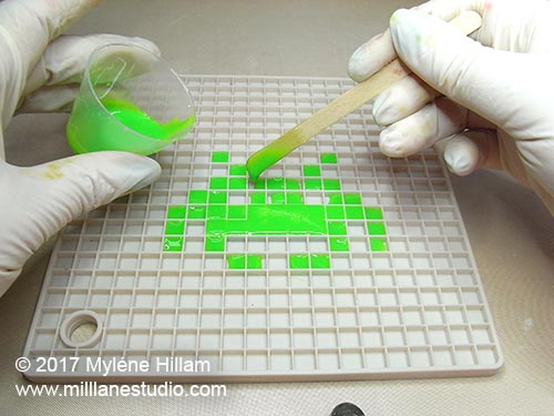 Pouring bright green resin into the squares of the silicone trivet in the shape of a space invader